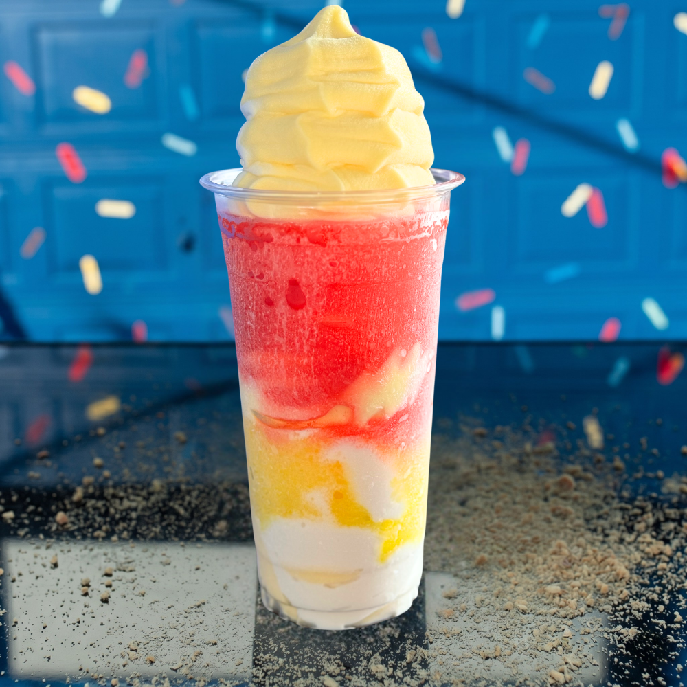 Colorful layered soft-serve sundae in a clear cup against a blue background