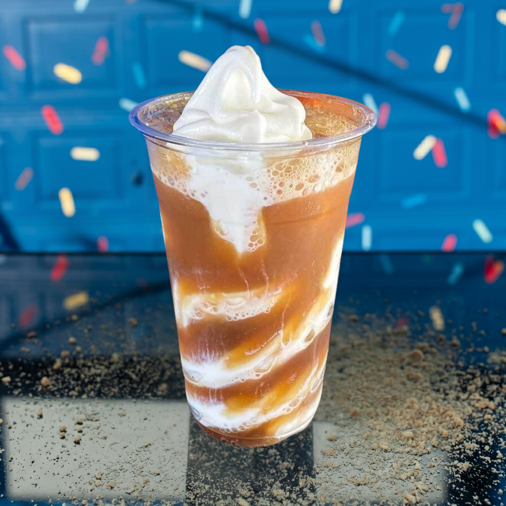 Soft-serve ice cream in a clear cup with caramel swirls, on a textured ledge with a blue backdrop