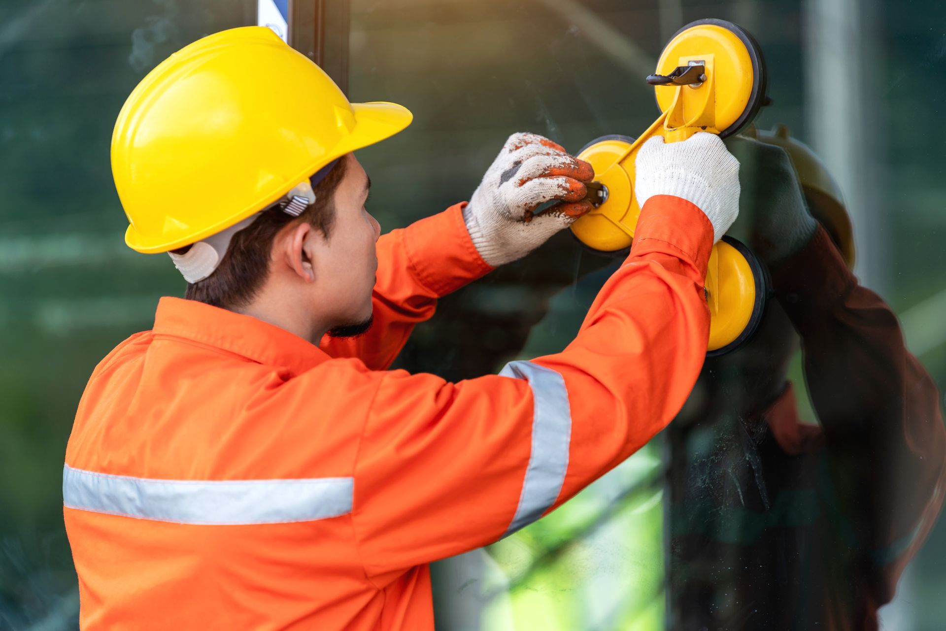 Construction worker using suction cups for window glass repair, wearing safety gear.