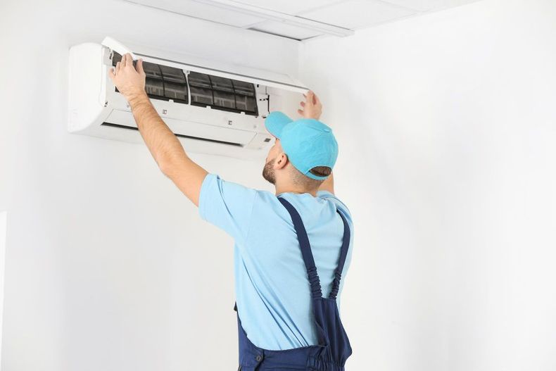 Technician repairing a wall-mounted air conditioner with the cover open.