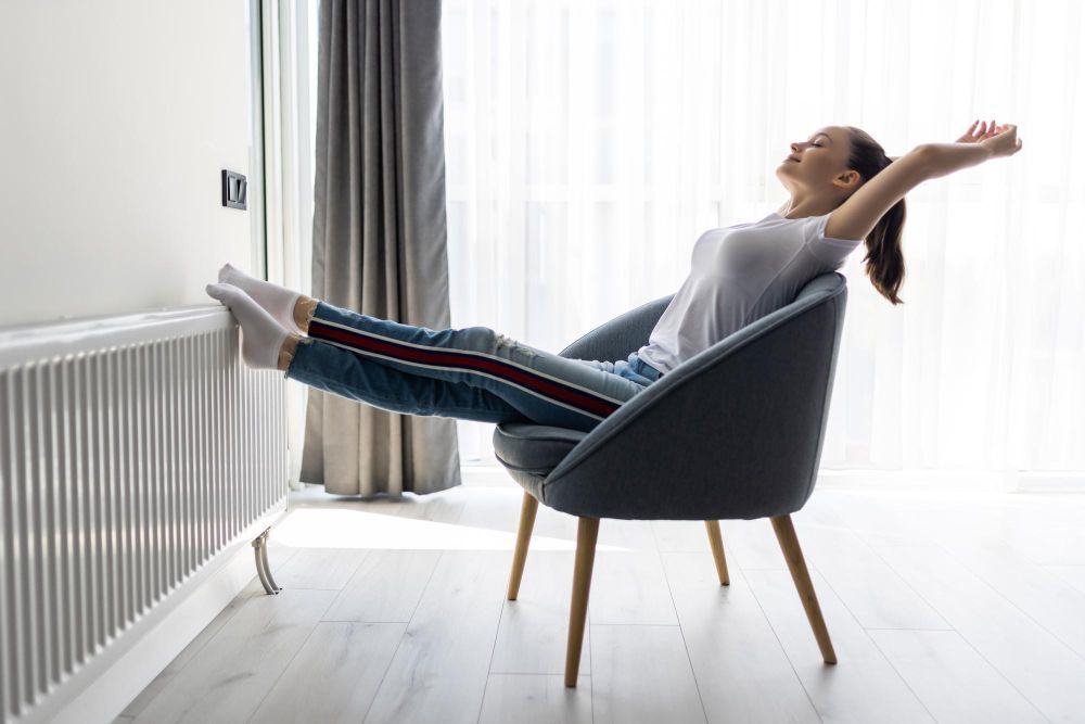 Person reclining in a chair with feet on a radiator, stretching in a bright living room