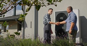 Two men shake hands outside a house near an outdoor HVAC unit.