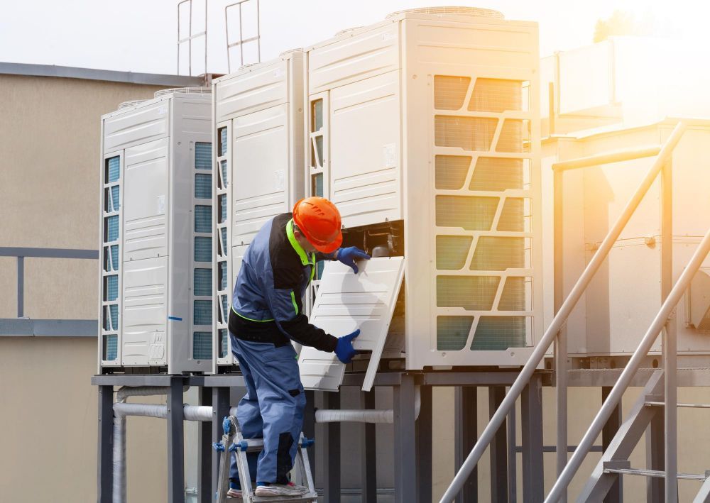 Worker in safety gear handling equipment beside outdoor industrial cooling units.