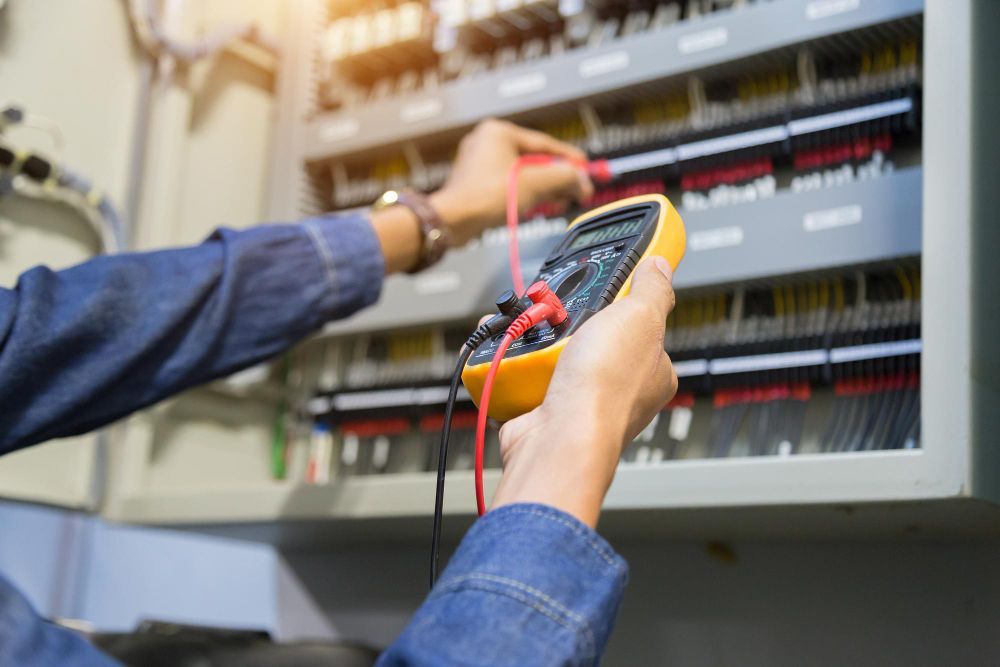 Technician using a digital multimeter to test wires in an electrical control panel