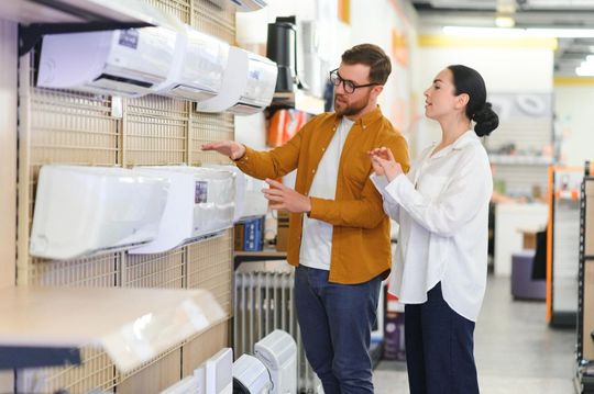 Two people examining wall-mounted air conditioners in an appliance store