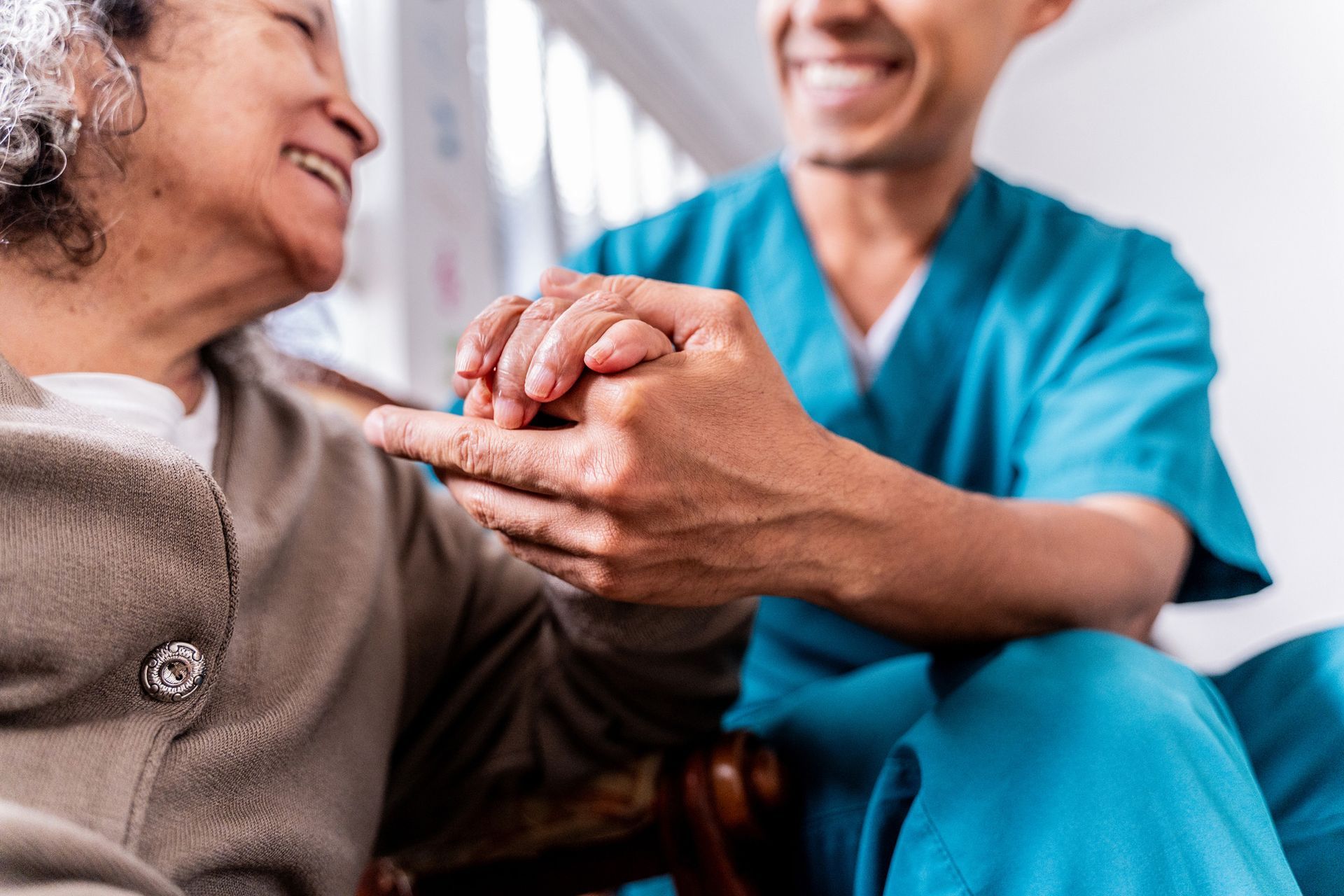 Caregiver holding hands with an elderly woman; both are smiling.
