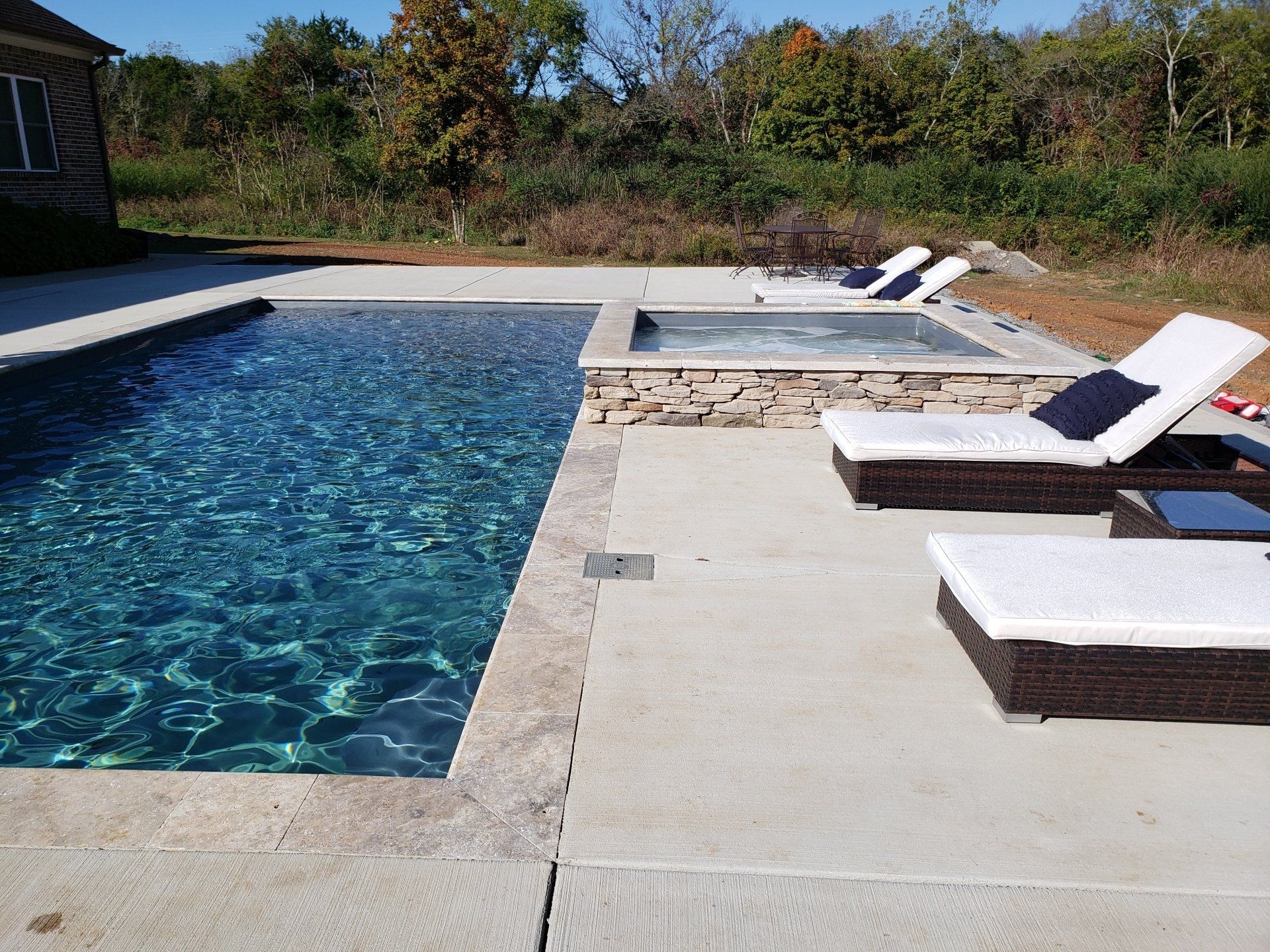 A large swimming pool is surrounded by lawn chairs and a hot tub.