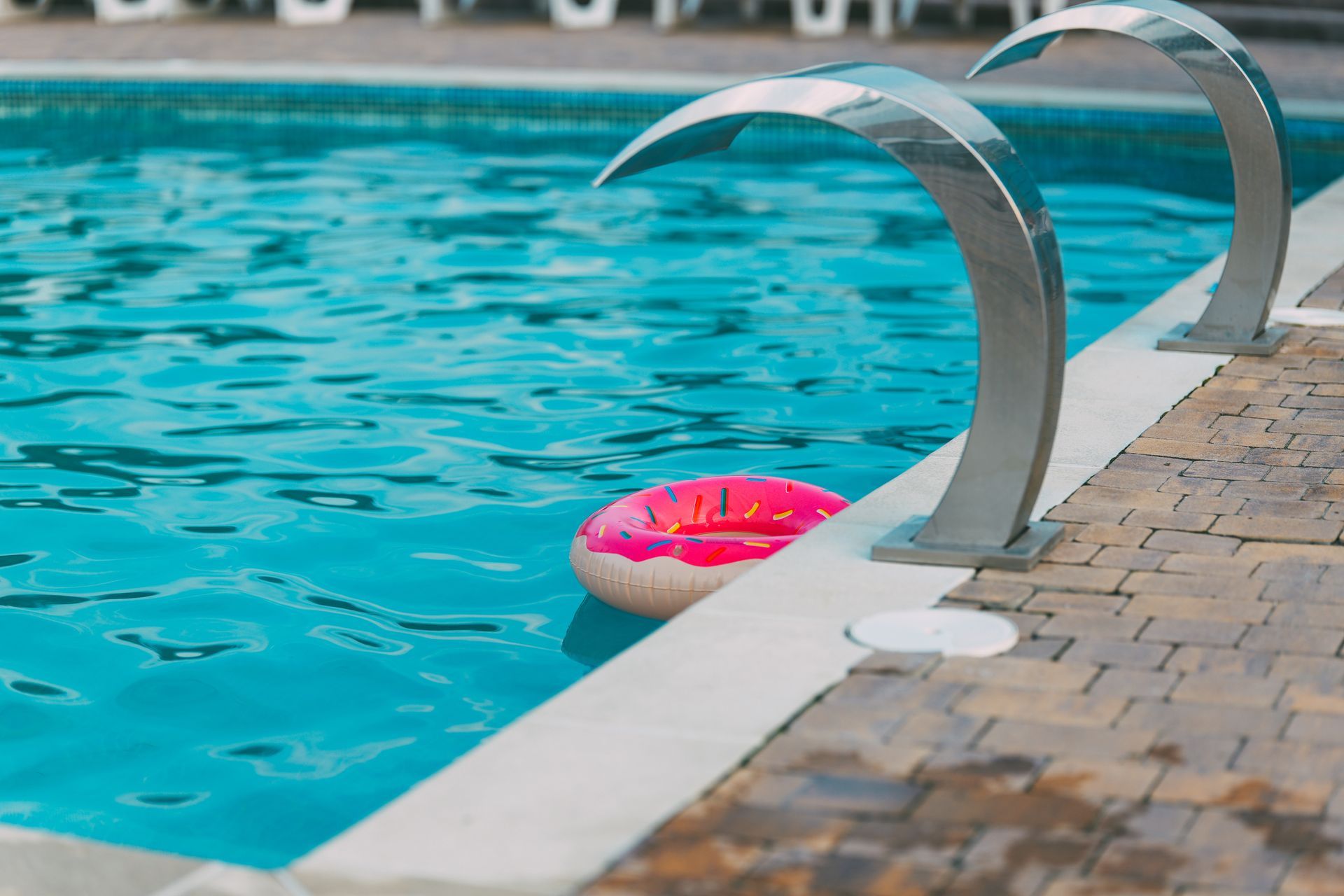 A pink donut pool float in a turquoise pool with silver water fountains.