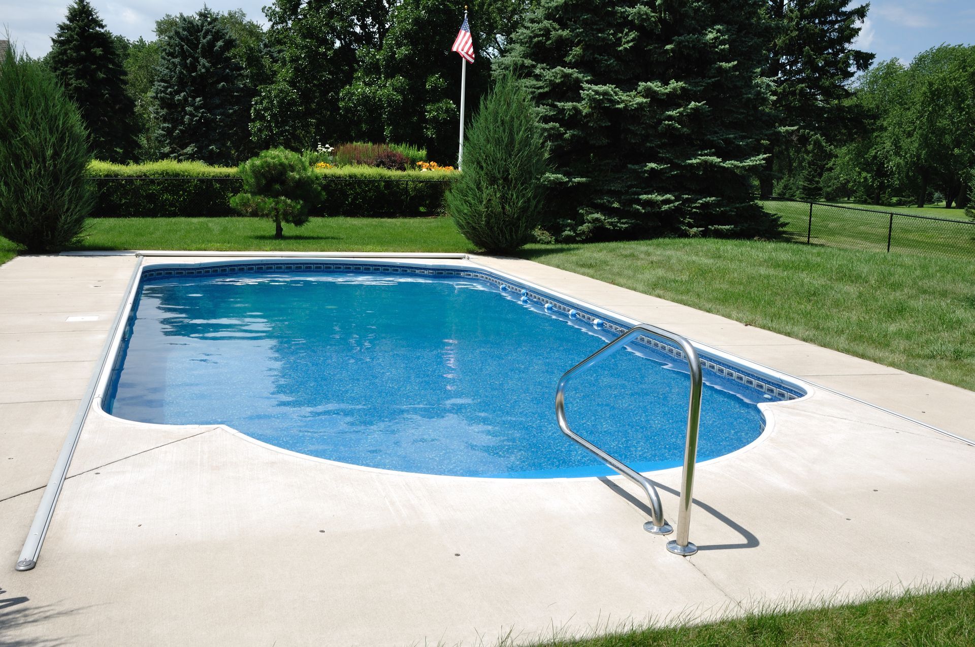 Backyard swimming pool with a concrete deck, steps, and green lawn under a sunny sky