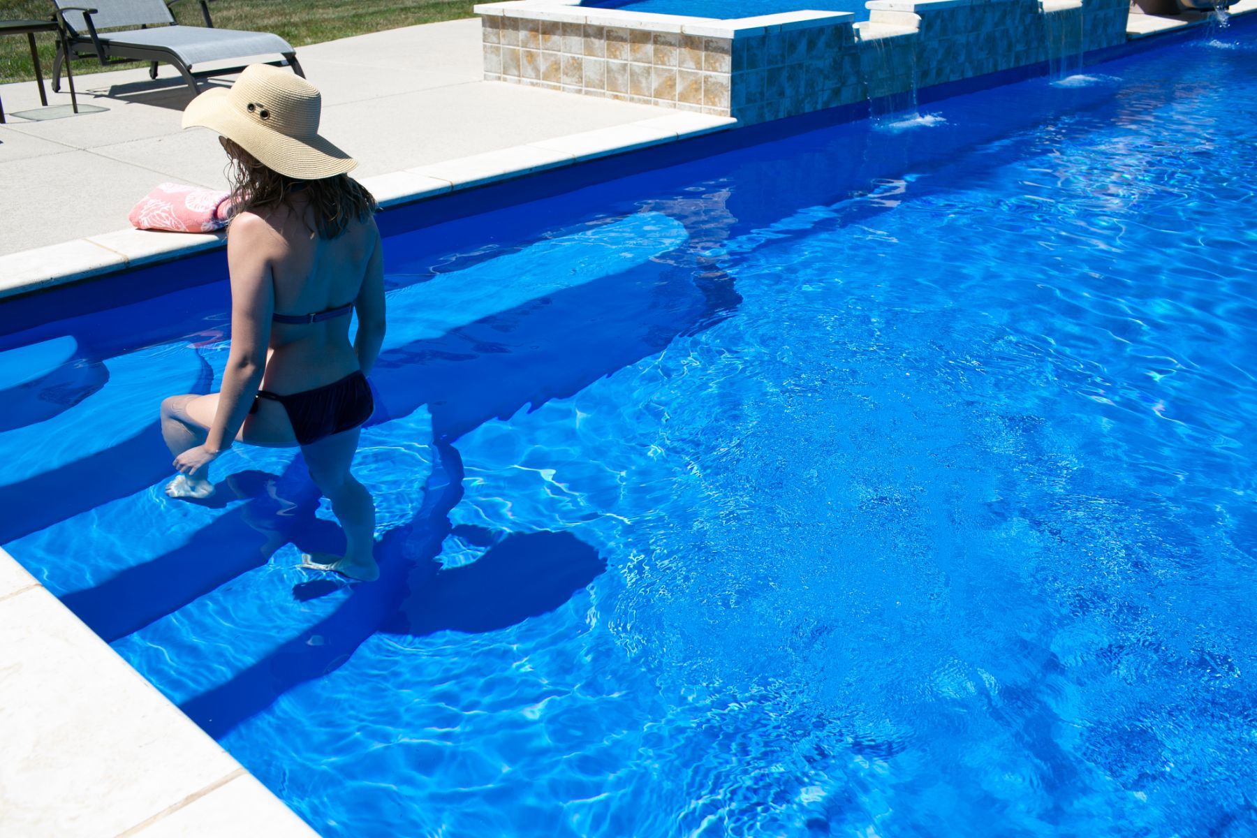 A woman in a bikini and hat is standing in a swimming pool.