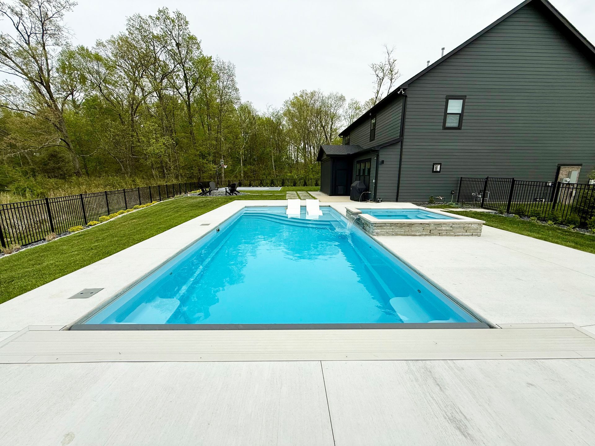 Backyard pool with bright blue water beside a gray house and white deck