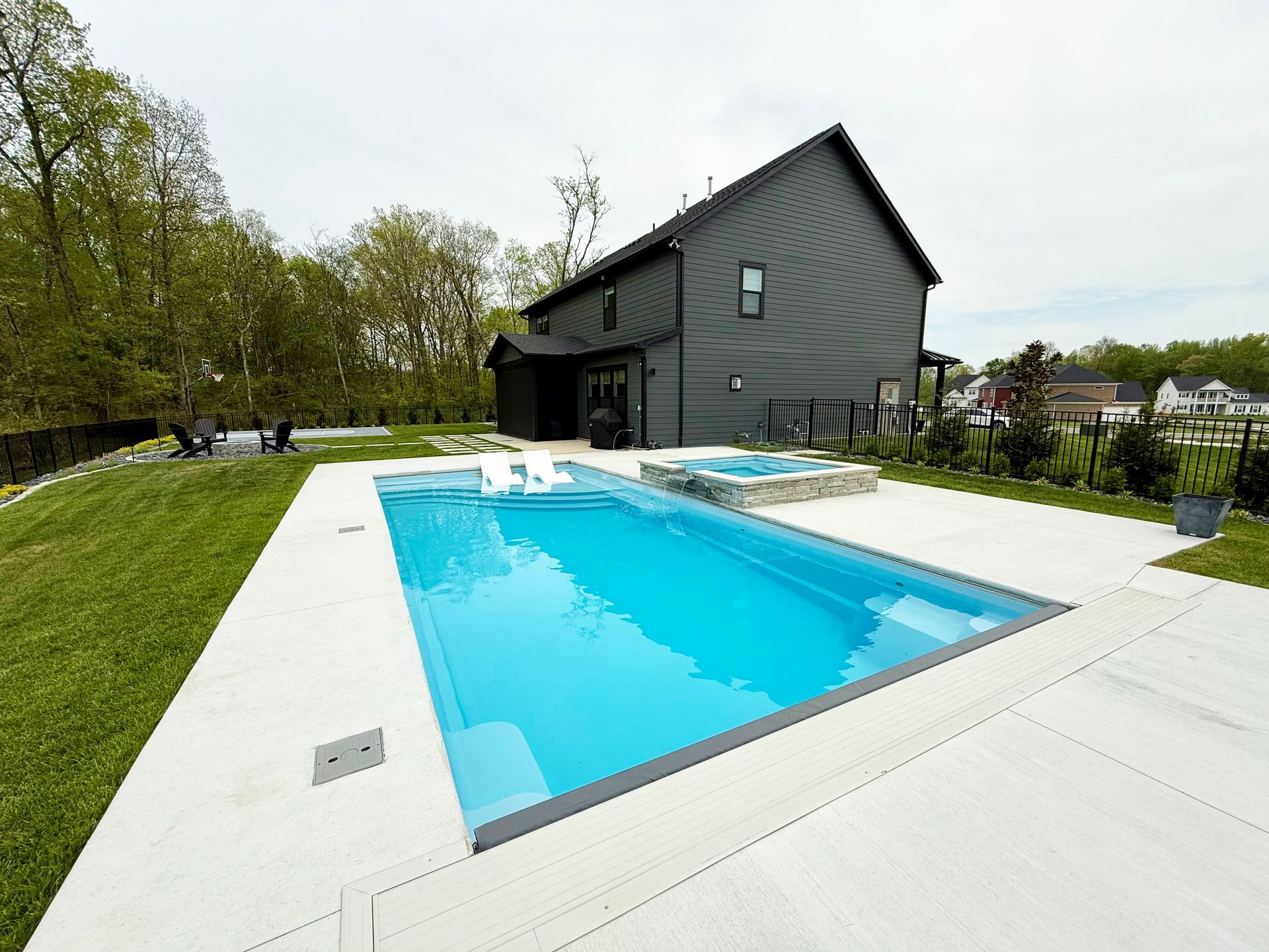 Backyard with a blue swimming pool beside a dark house and green lawn