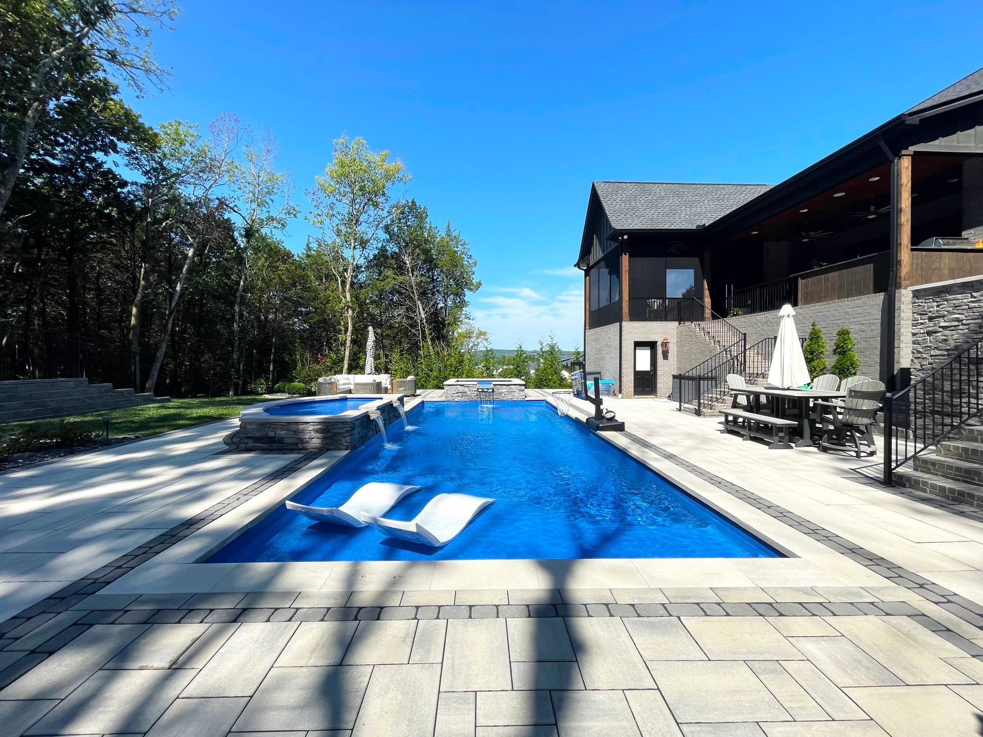 Backyard oasis with Aspen pool, spillover spa, and lush wooded view designed by Majestic Swim in Murfreesboro.