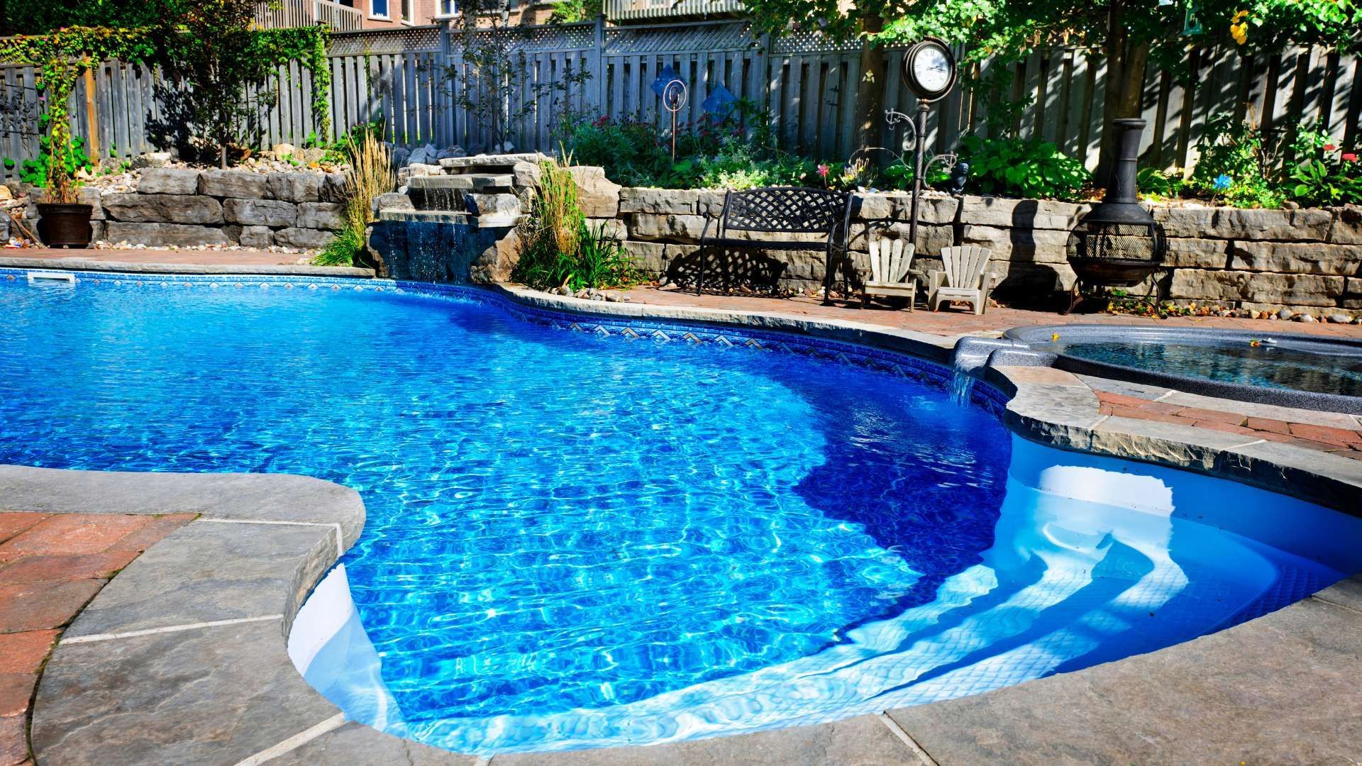Backyard swimming pool with blue water, stone deck, and lounge chairs along a fence line
