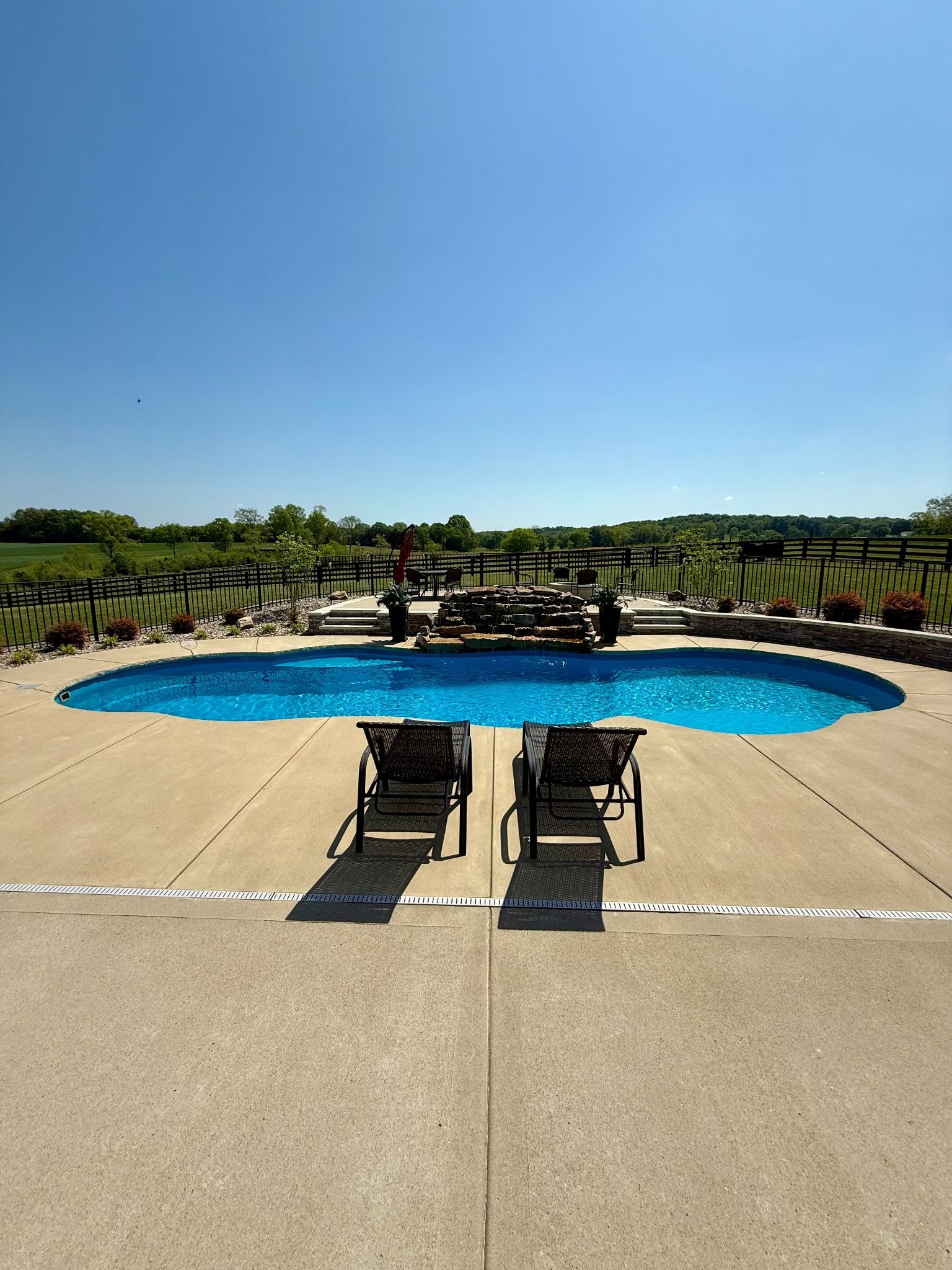 Centered view of backyard pool in Lascassas with two lounge chairs and natural rock waterfall