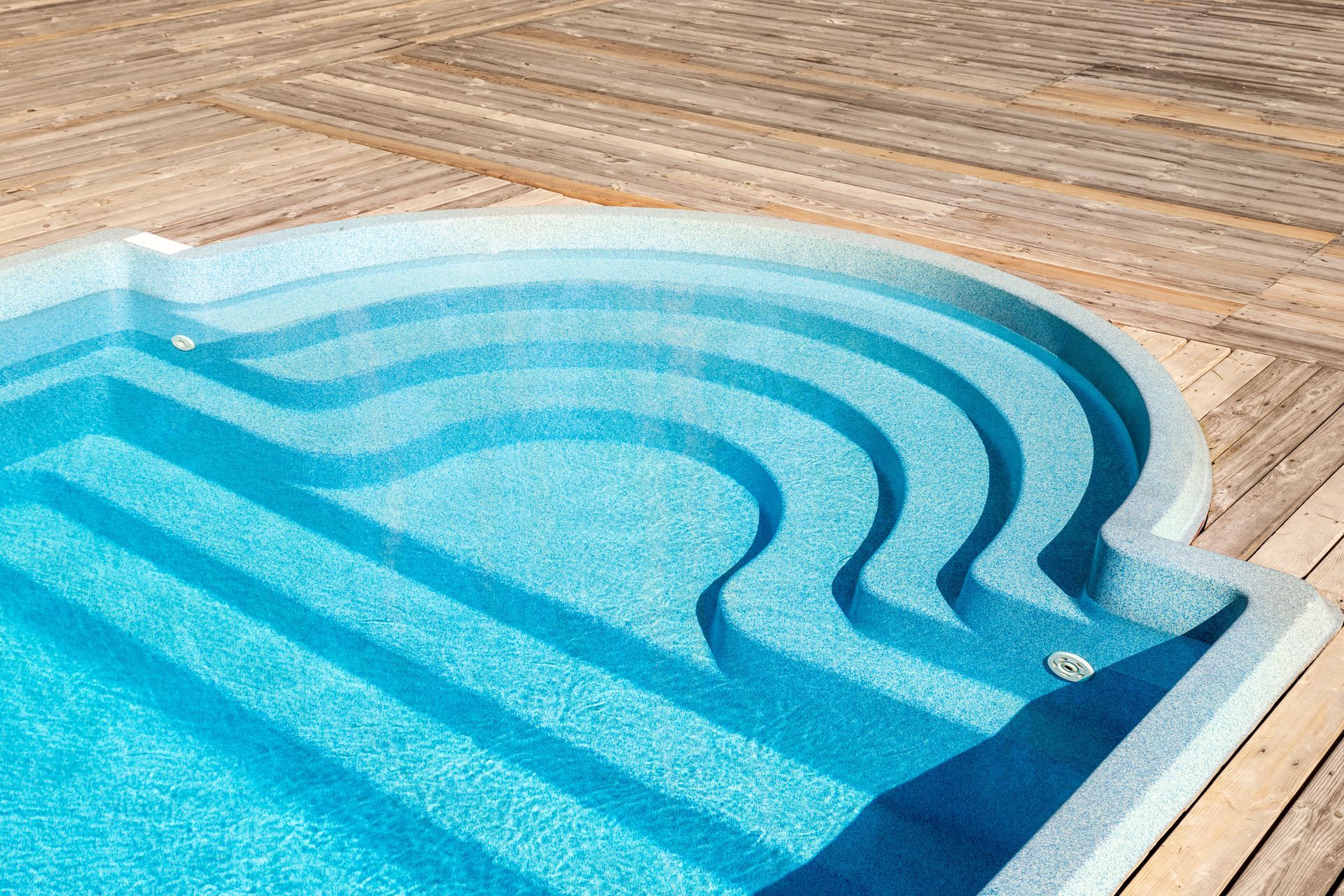 Turquoise swimming pool with curved steps beside a wooden deck