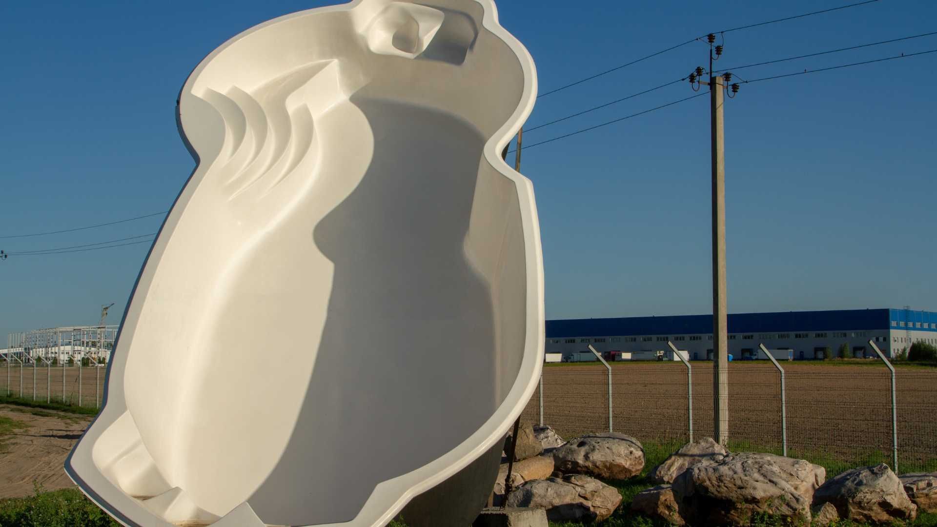 White abstract owl sculpture outdoors near a fence and utility poles under a clear blue sky