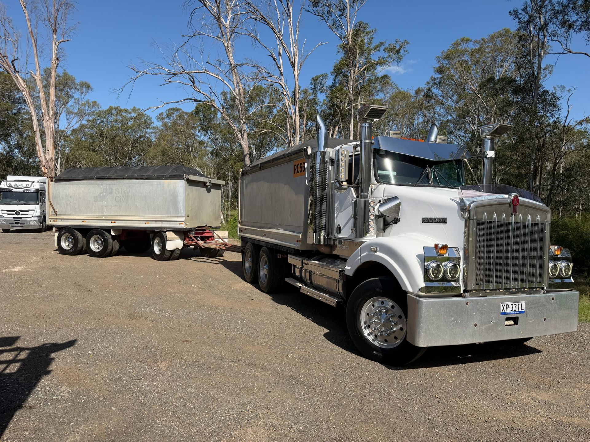 White truck with trailer loaded with dark material, parked outdoors on gravel — Azza's Mini Diggers in Port Macquarie, NSW