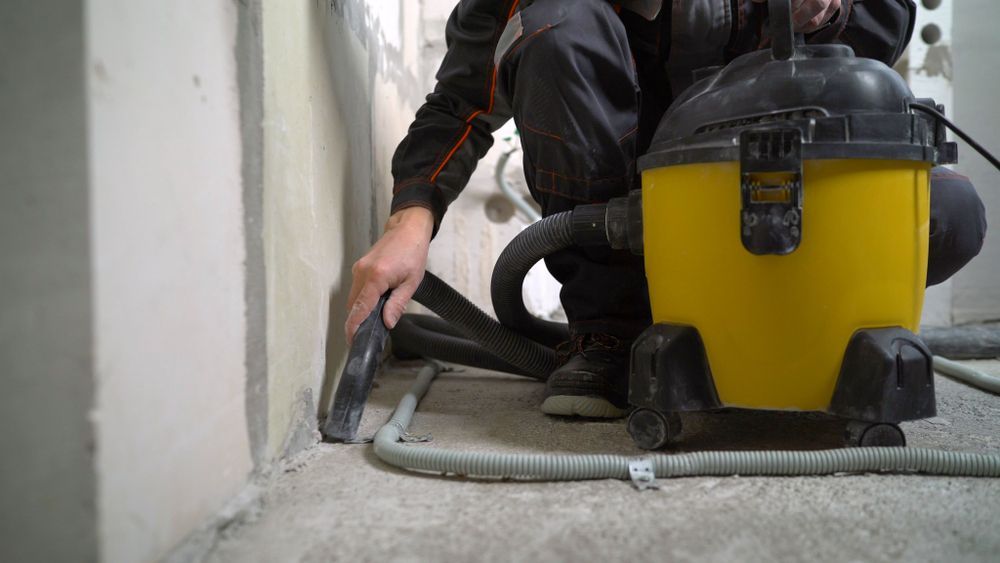 Person Using a Yellow Shop Vacuum to Clean Dust Along a White Wall — Restore All Qld in Kingaroy, QLD