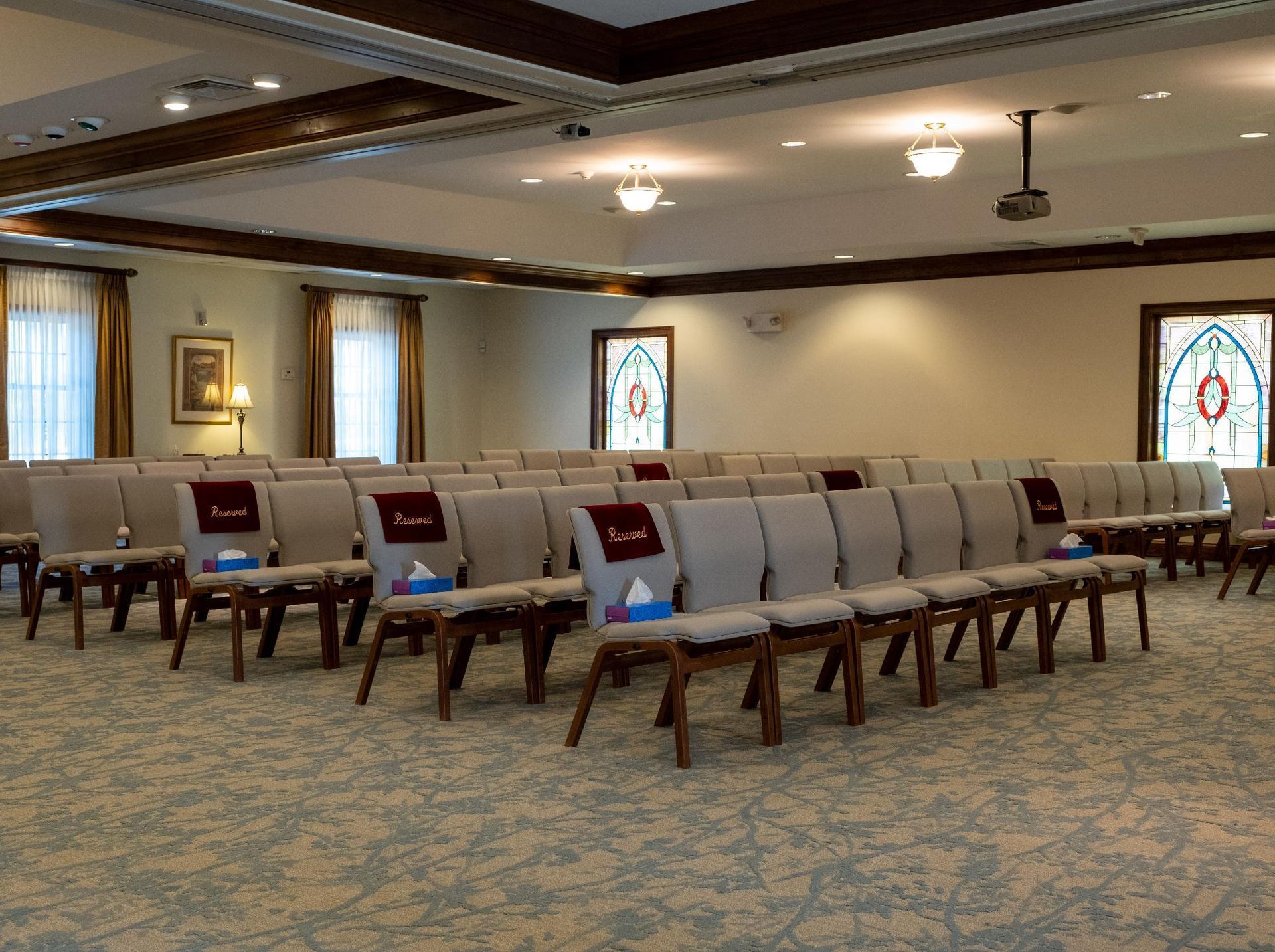 Empty room with rows of chairs, stained glass windows, and a projector.