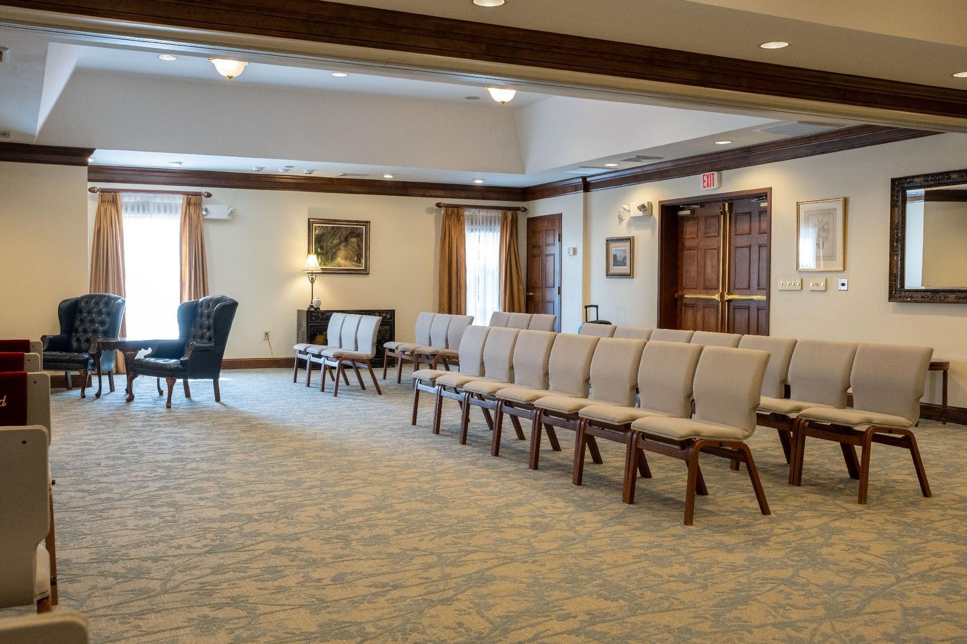 Rows of chairs face a doorway in a carpeted room with neutral colors, possibly a chapel.