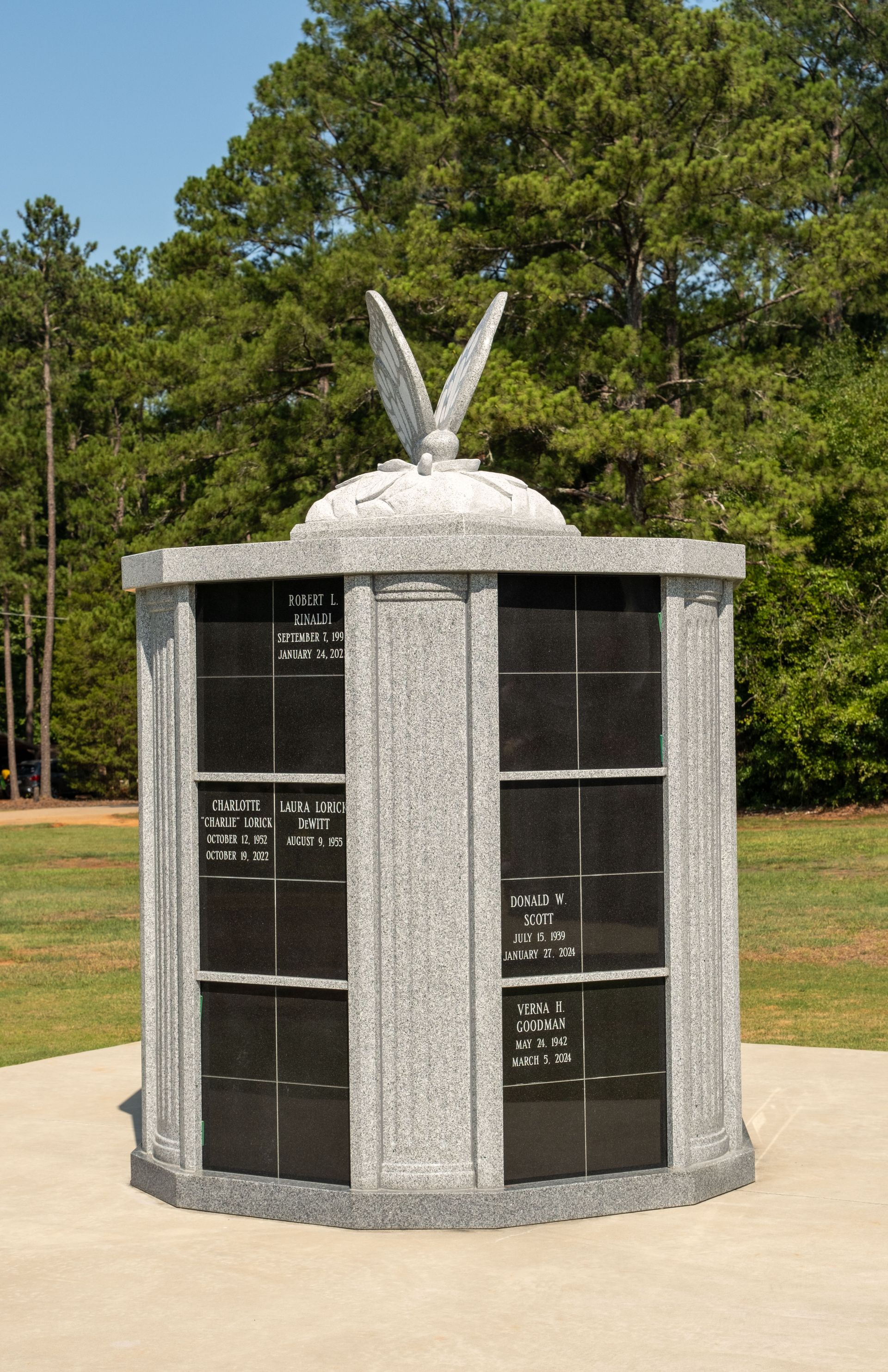 Granite columbarium with black niches, topped with eagle sculpture, set on a sunny, grassy lawn.