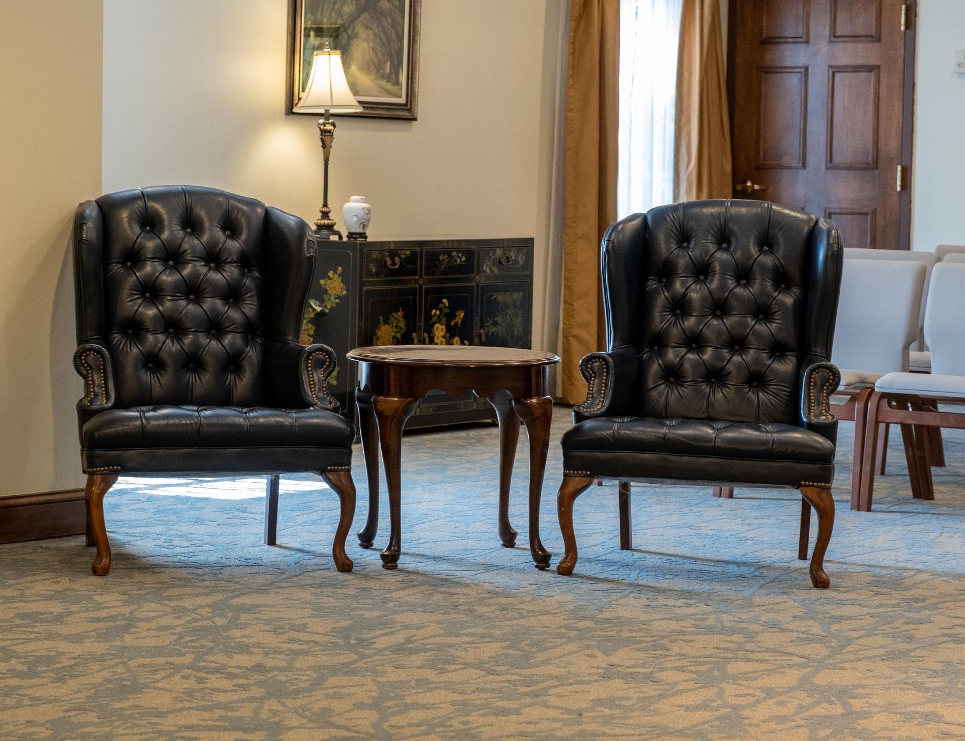 Two black leather wingback chairs face each other with a small table between them in a room with a light rug.