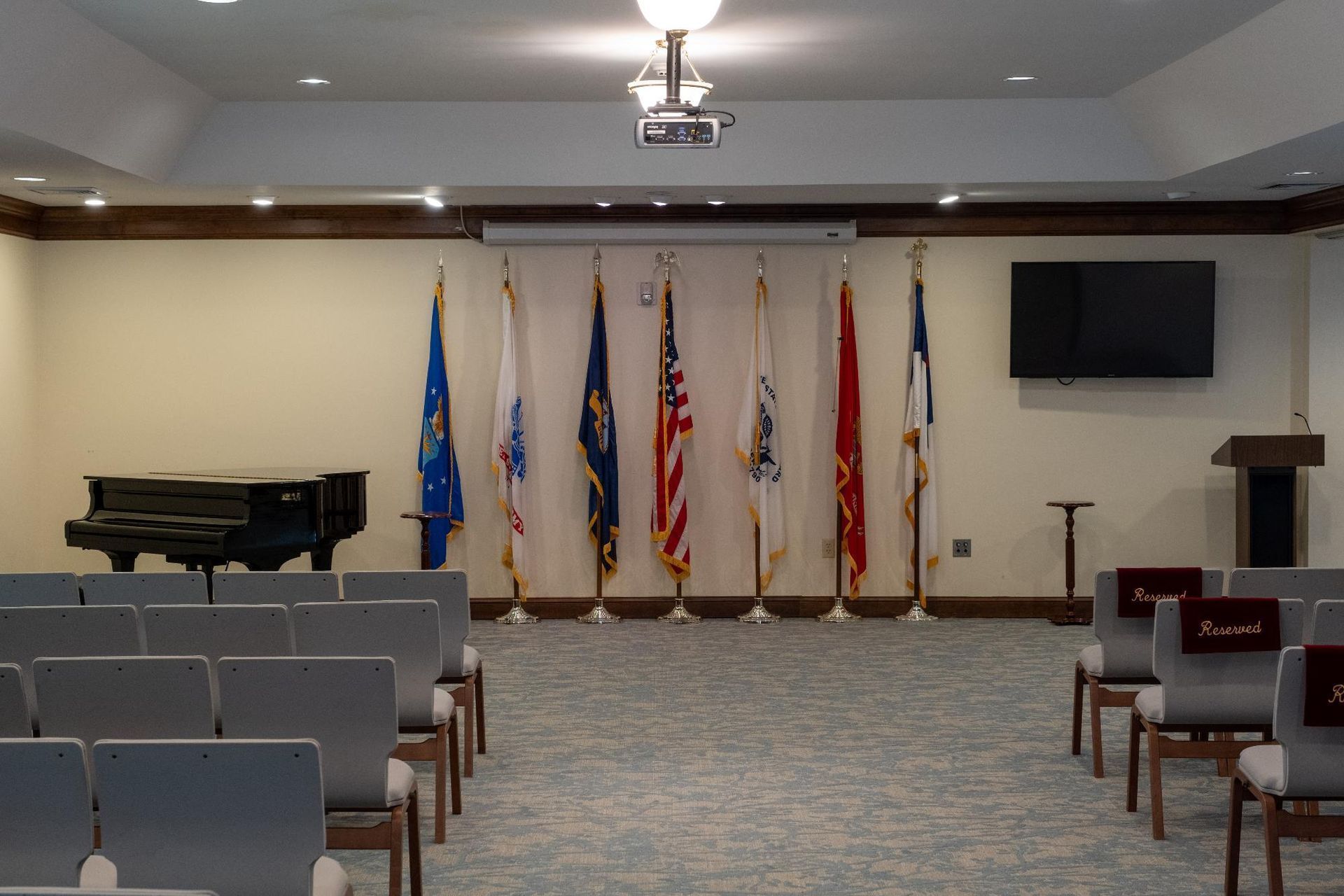 Ceremony room with flags of military branches, a piano, and chairs.