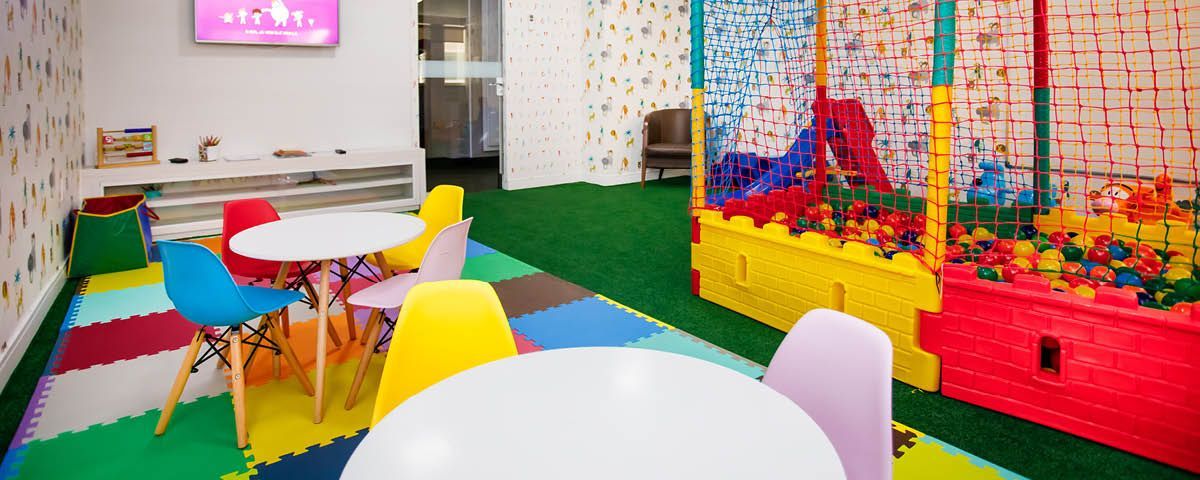 Sala infantil com mesas e cadeiras e piscina de bolinhas.