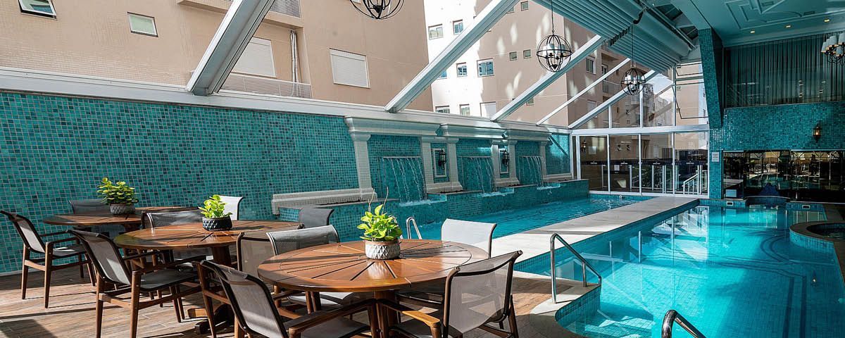 Uma piscina com mesas e cadeiras em frente.