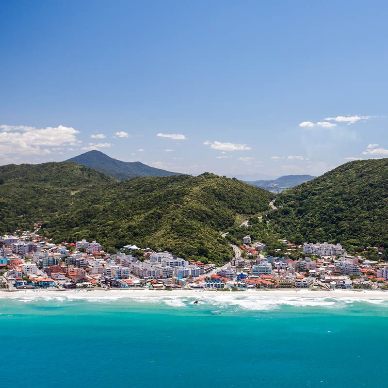 Cidade litorânea cercada por morros e mar azul.