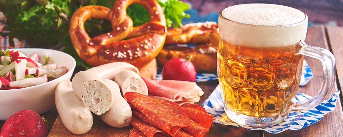 Uma mesa coberta com pretzels, salsichas e um copo de cerveja.