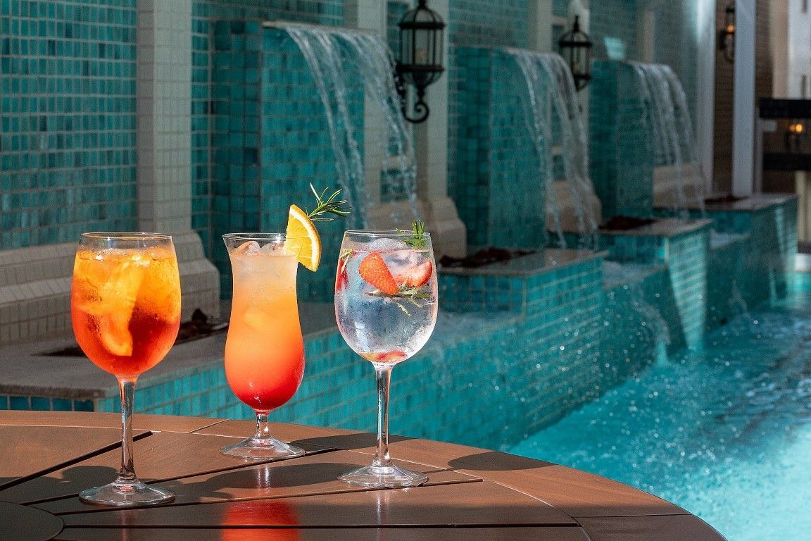 Três bebidas estão sobre uma mesa ao lado de uma piscina.