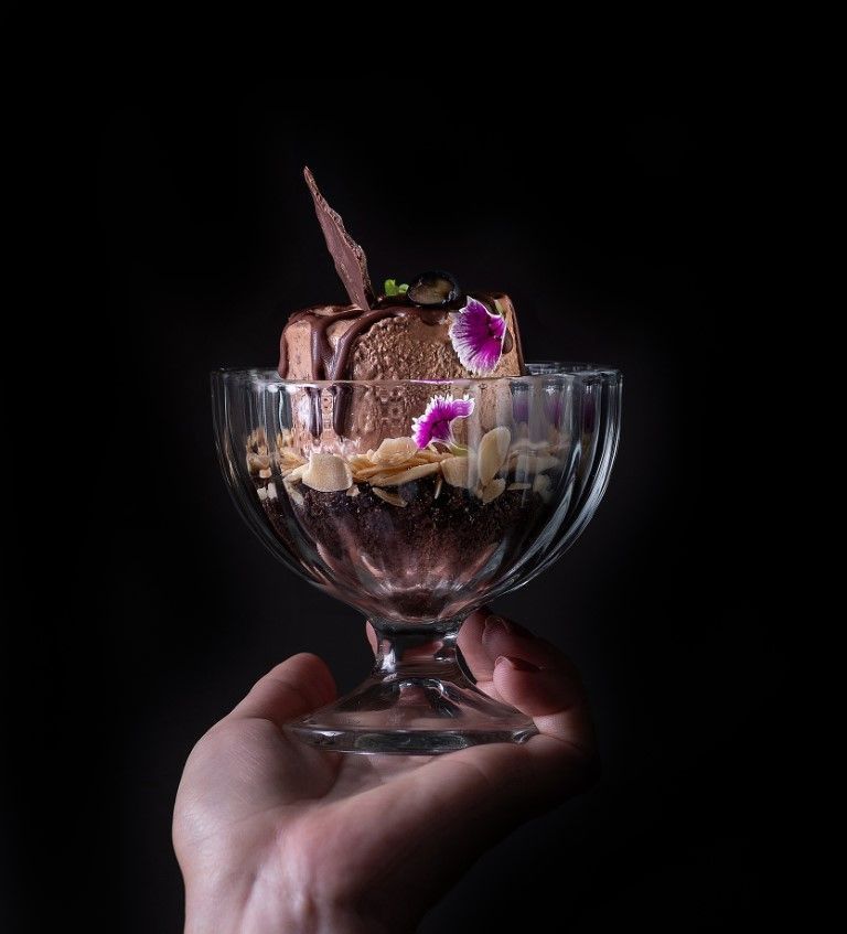 Uma pessoa está segurando uma tigela de vidro com sorvete de chocolate.