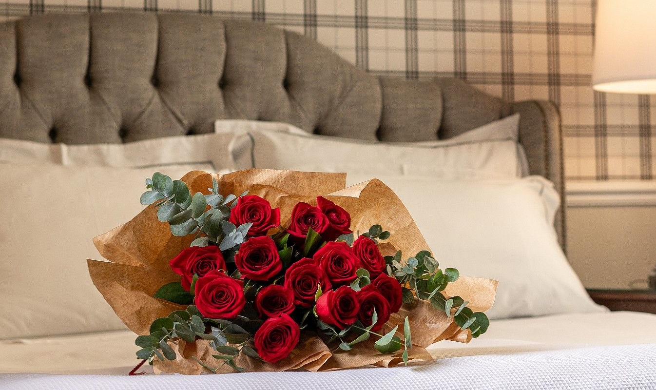 Um buquê de rosas brancas está em uma cama ao lado de um abajur.