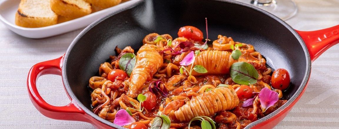 Uma panela cheia de macarrão e tomate está sobre uma mesa.