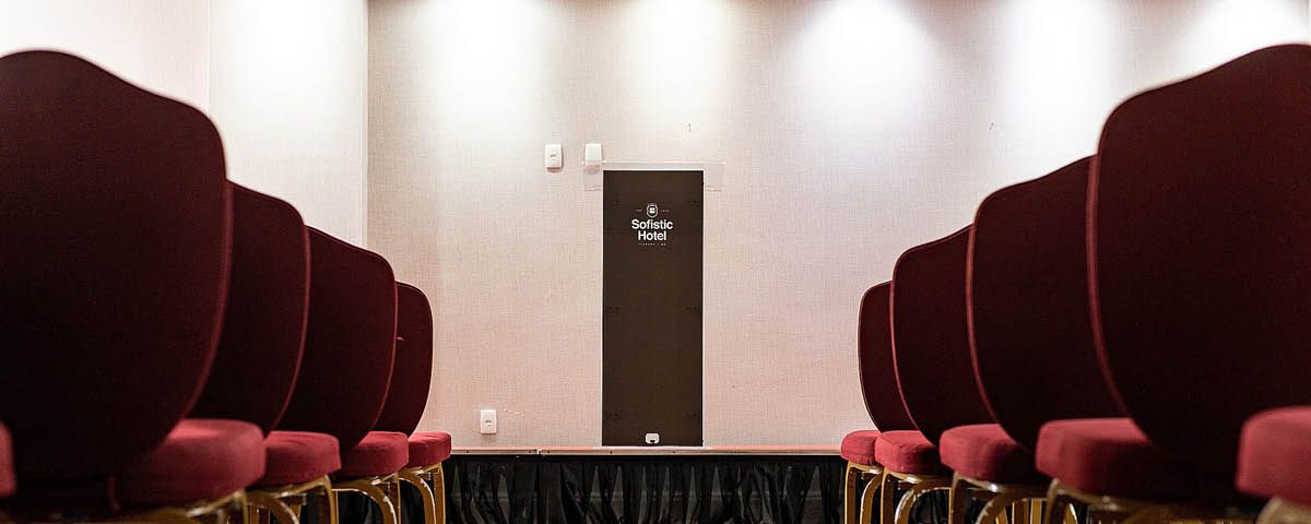 Uma fileira de cadeiras vermelhas em um auditório com uma porta ao fundo.