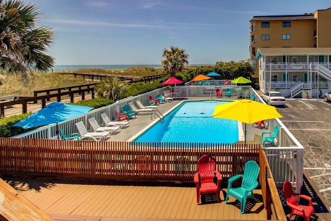 A large swimming pool surrounded by chairs and umbrellas in front of a building.