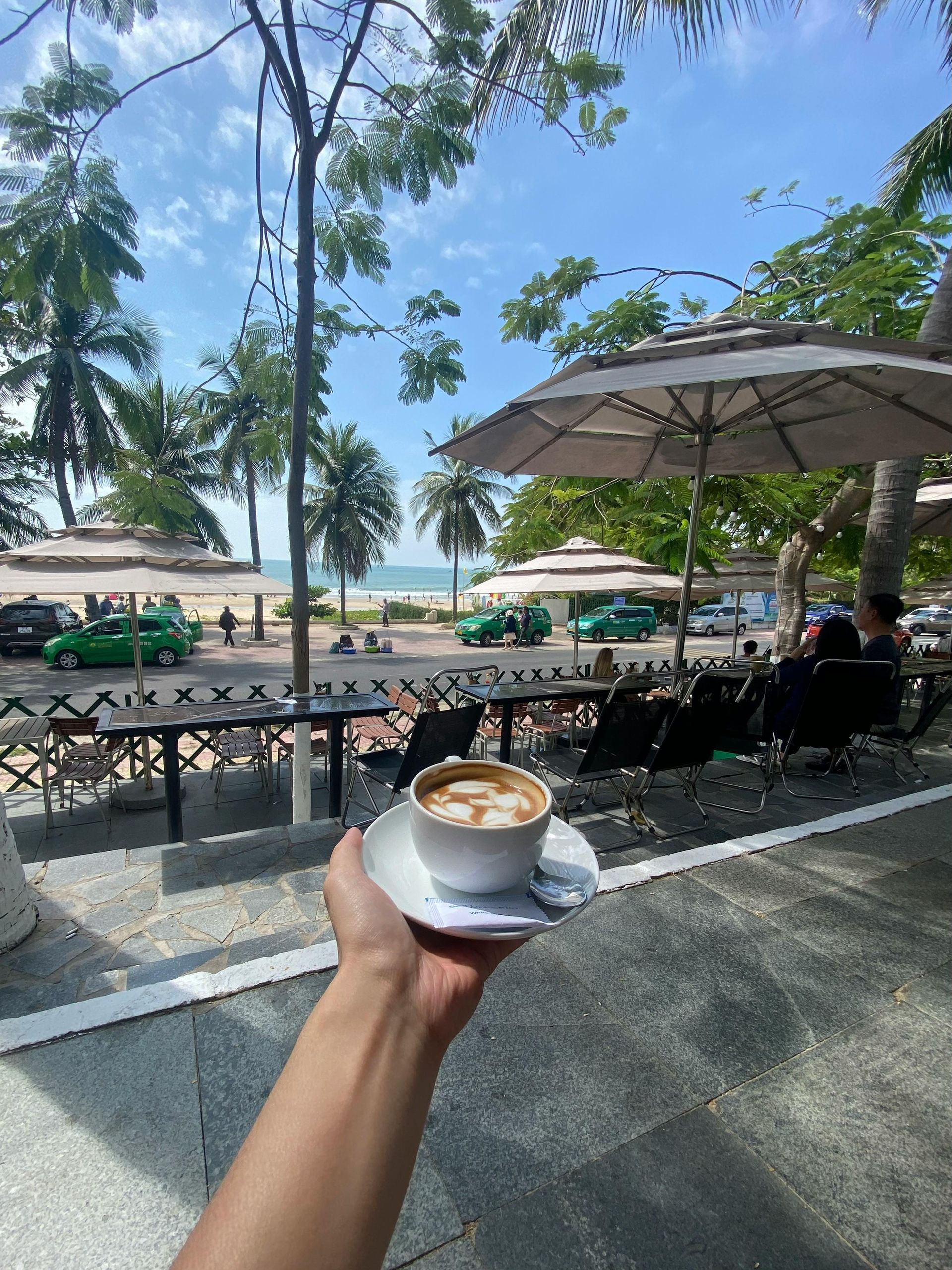 A person is holding a cup of coffee in front of a beach.