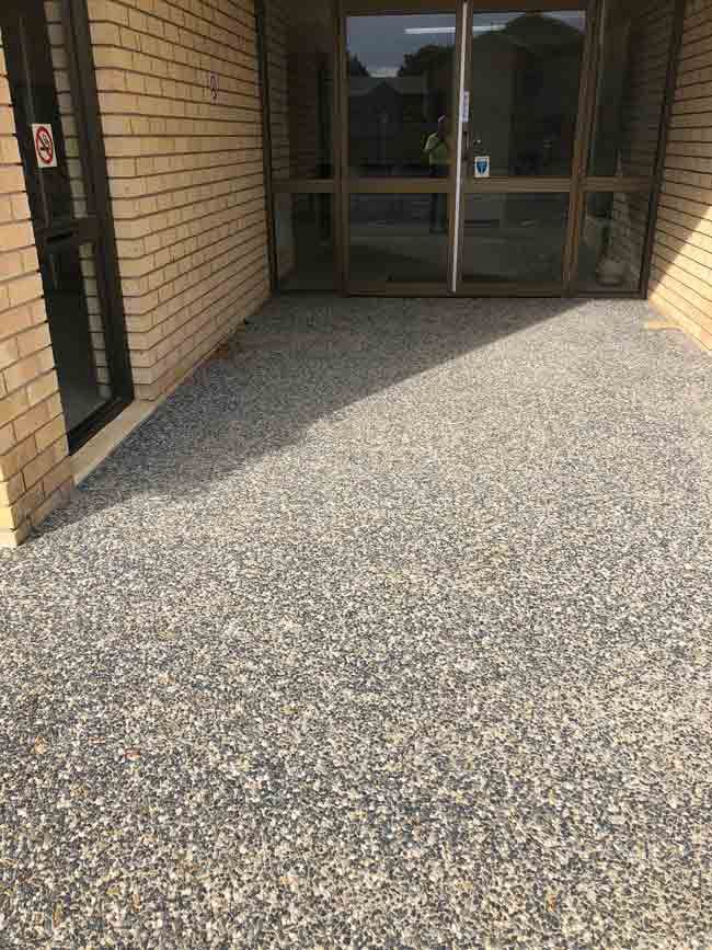 Gravel-Like Patio Outside a Building with Glass Doors and Brick Walls — Wieland Concreting in Rockhampton, QLD