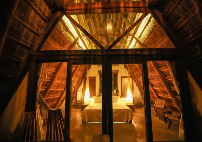 Acogedora habitación de madera con estructura en forma de A, iluminación cálida, cama y cortinas bajo vigas inclinadas.