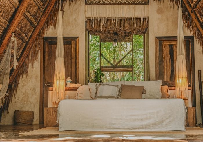 Acogedora habitación tropical con una cama grande, vigas de madera y cortinas transparentes con vistas a la vegetación.