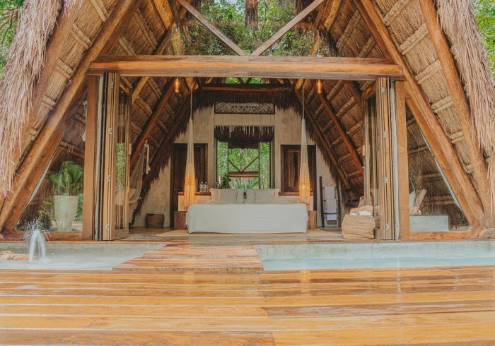 Pabellón al aire libre con techo de paja, vigas de madera, altar blanco y suelo de madera pulida junto a una piscina.