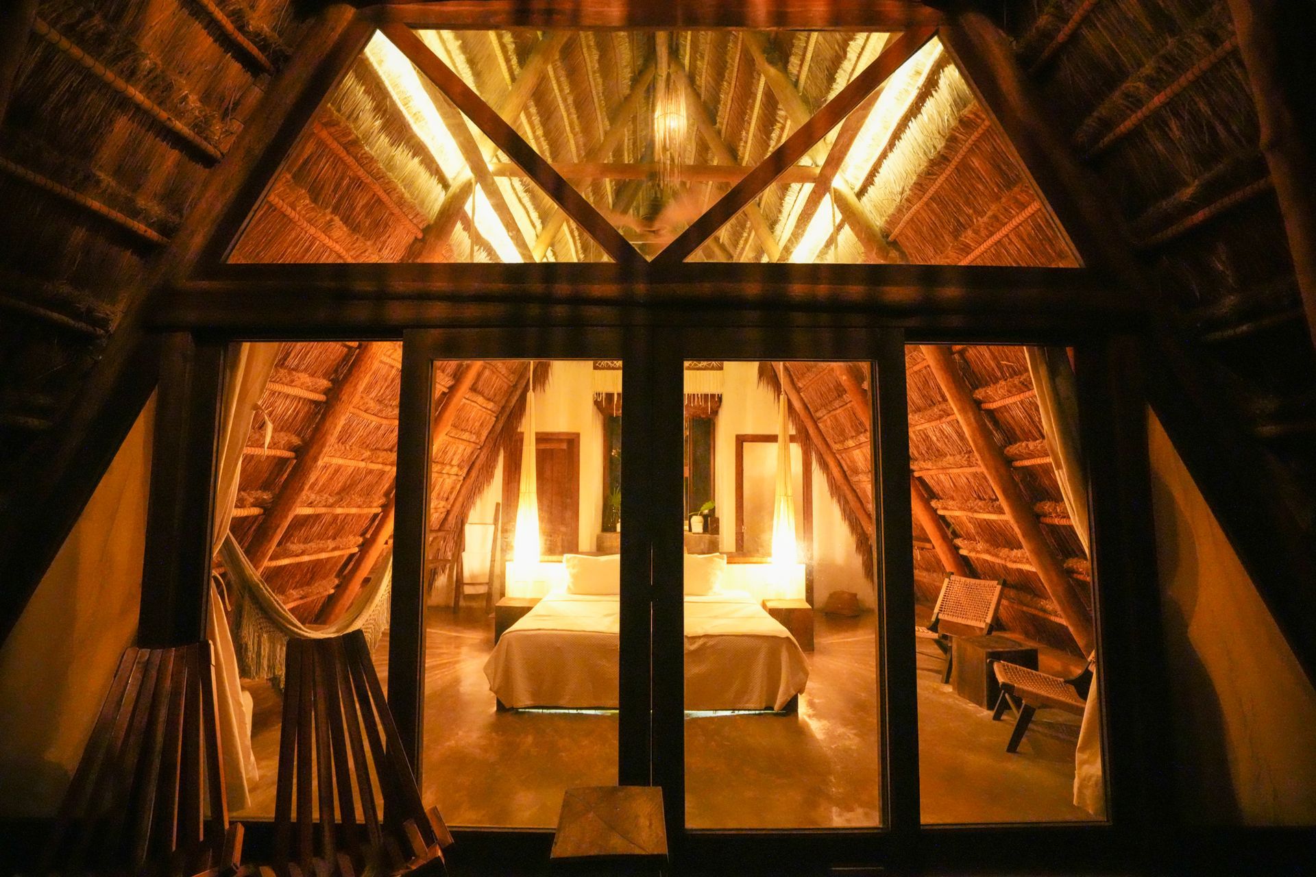 Interior acogedor de una cabaña con estructura en forma de A, con luces cálidas, vigas de madera y puertas de cristal.