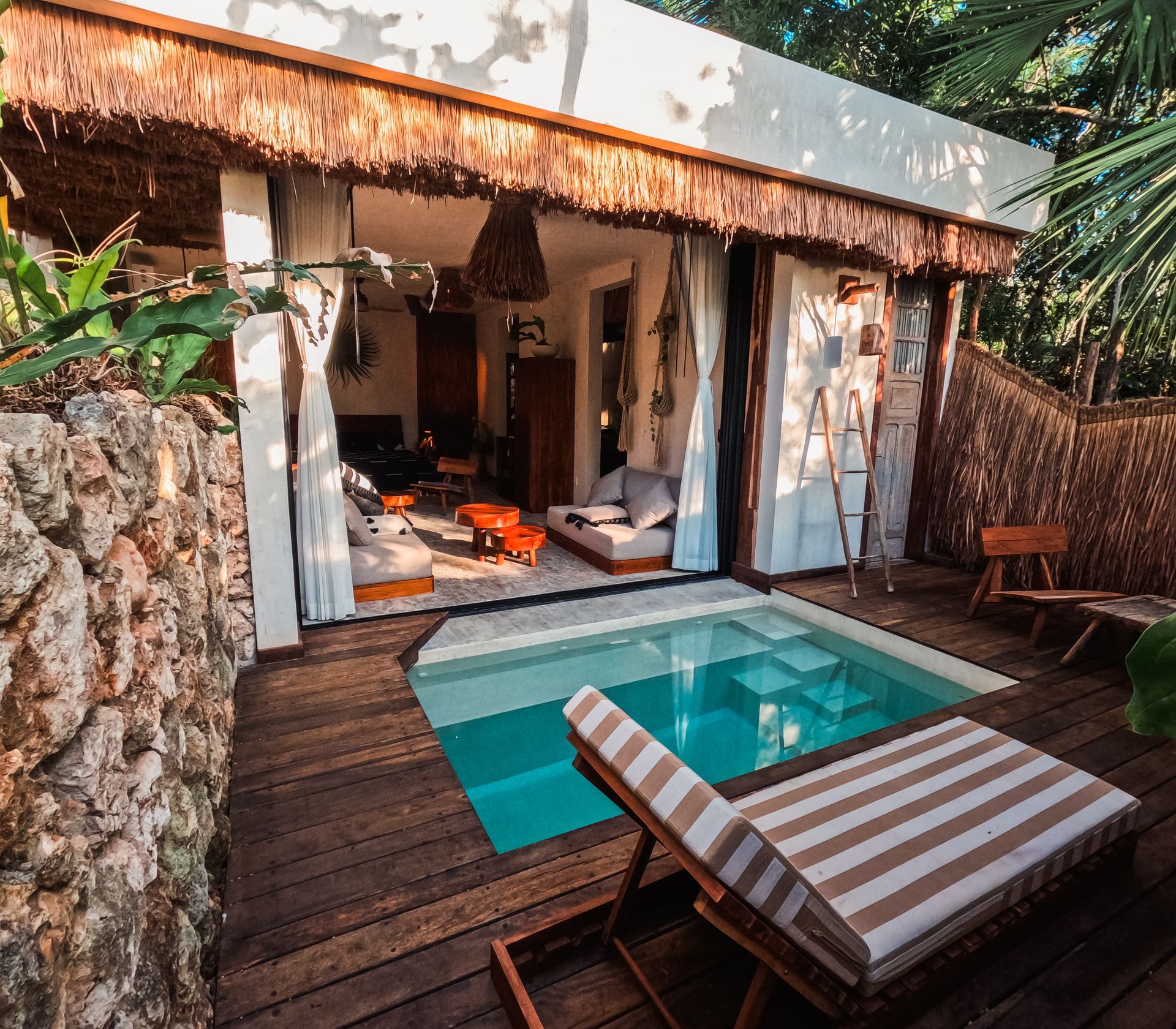 Pequeña terraza de villa tropical con una piscina diminuta y una tumbona a rayas, abierta a un interior acogedor.
