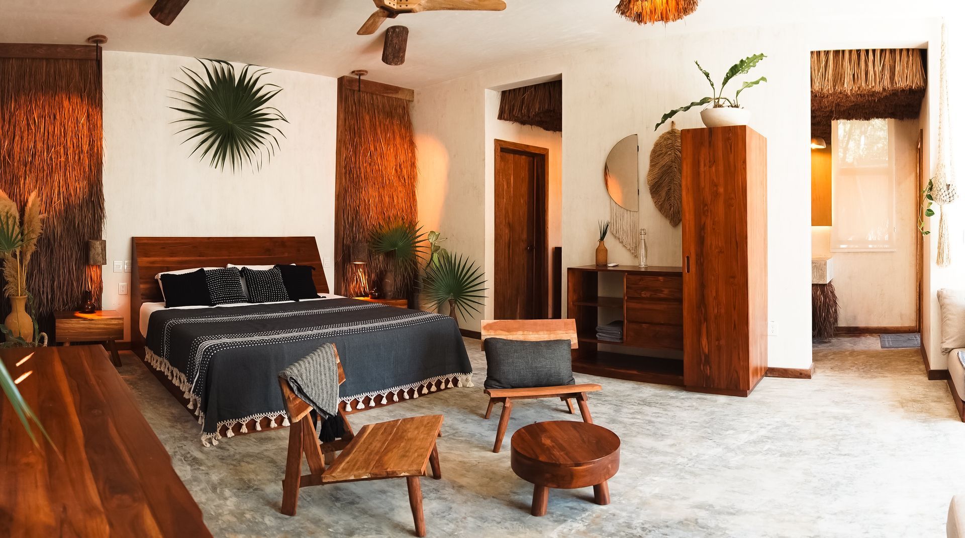 Acogedora habitación rústica con cama negra, sillas de mimbre, detalles de madera y abundante luz natural.