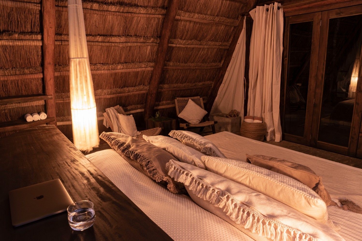 Acogedora habitación rústica con cama, lámpara cálida y paredes de paja por la noche.