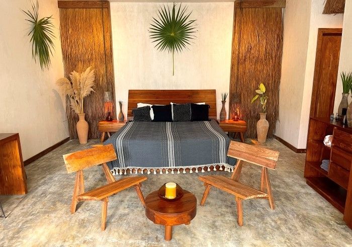 Habitación acogedora con una cama oscura, decoración de madera y dos sillas frente a una mesa pequeña.