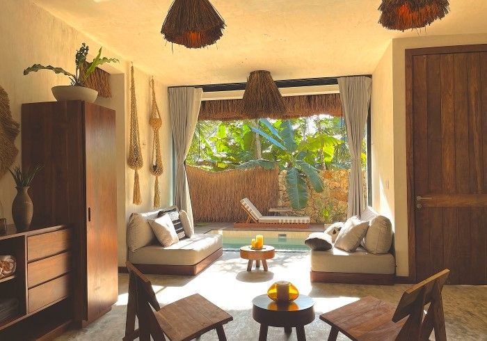 Acogedora sala de estar soleada con sillas de mimbre, muebles de madera y vista a un patio abierto con exuberante vegetación.