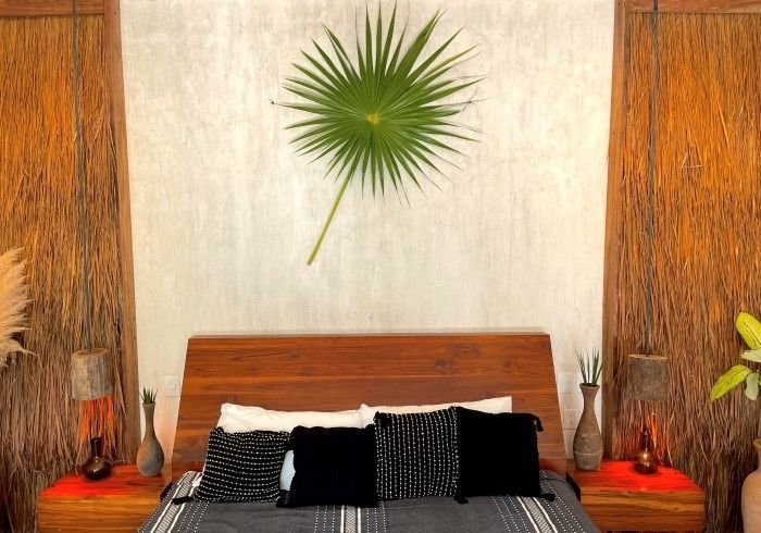 Dormitorio elegante con cabecero de madera, ropa de cama en blanco y negro y decoración de pared con hojas verdes.